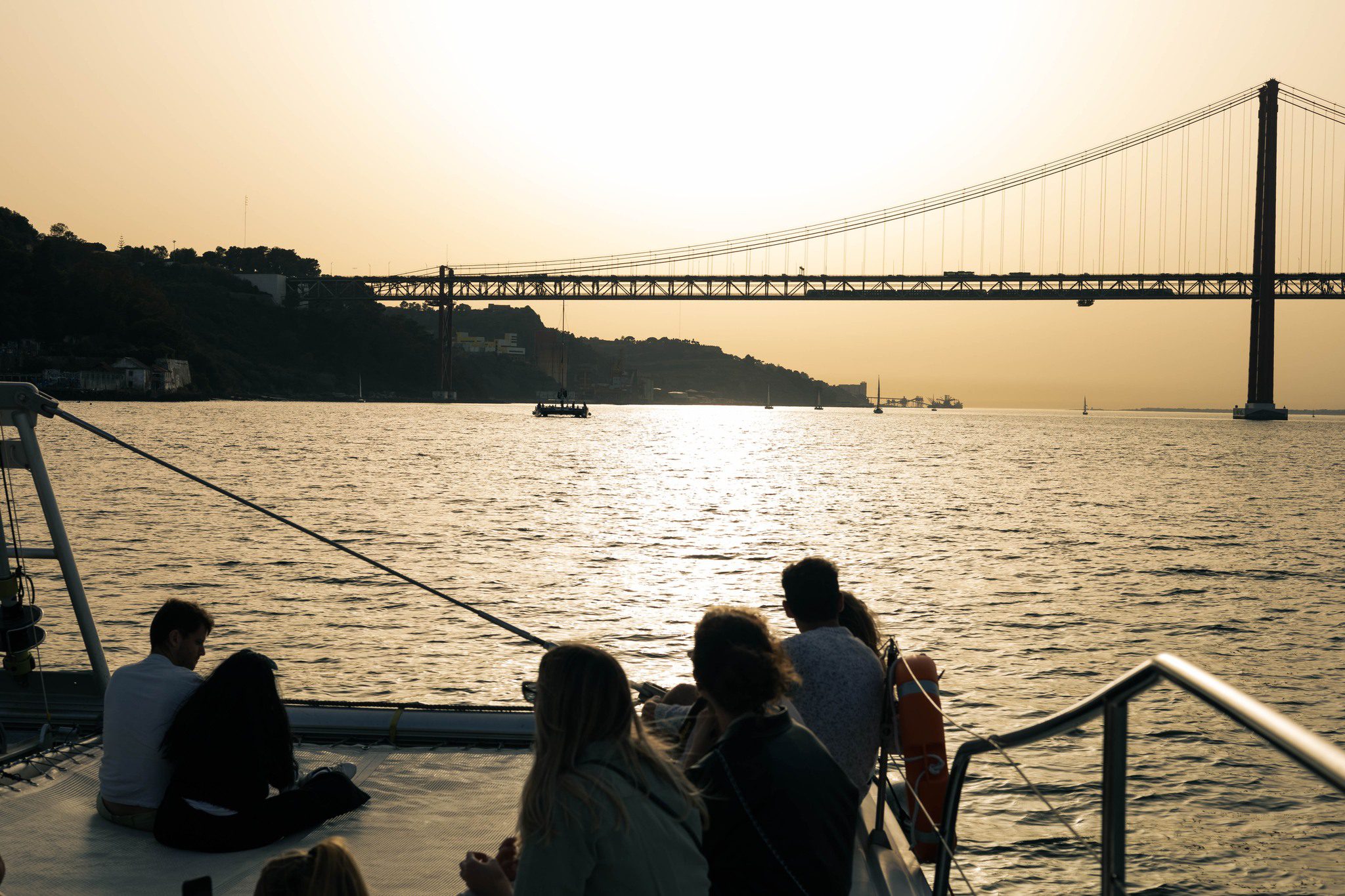 Gente disfrutando del atardecer en un barco bajo el puente de Lisboa