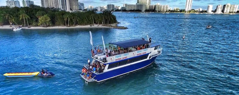 A large double-decker sightseeing boat cruising through the blue waters of Biscayne Bay Miami.