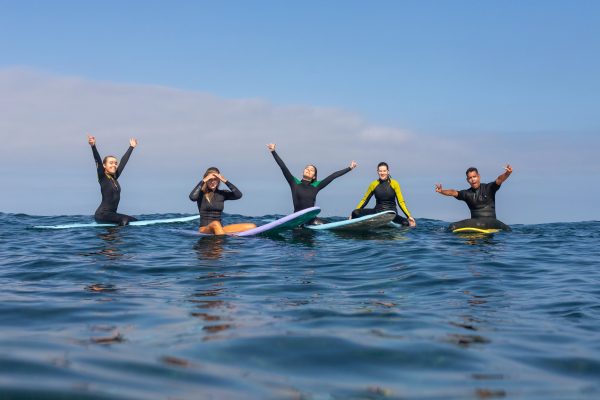 A group of happy beginners practicing surfing techniques on a sandy beach in Tenerife.
