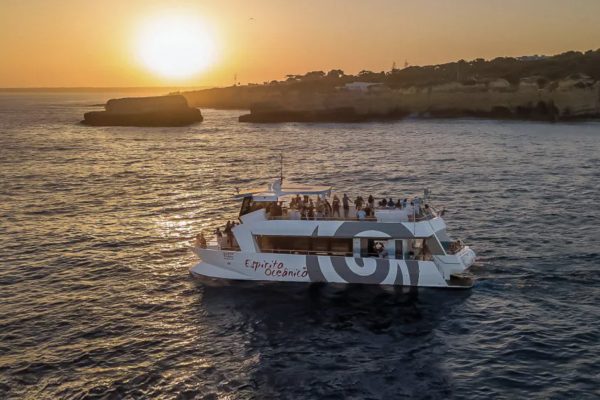 Large motro vatamaran with upper deck cruising along the Algarve coats during sunset