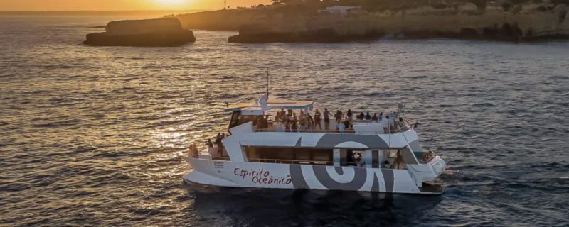 Large motro vatamaran with upper deck cruising along the Algarve coats during sunset
