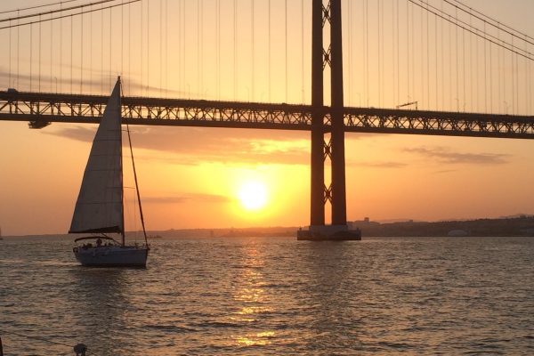 sailing boat under the 25th of April Bridge in Lisbon during sunset