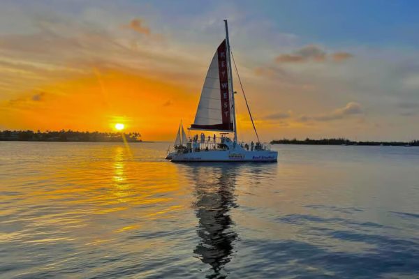 A large catamaran sailing at sunset in Key West with passengers on deck.