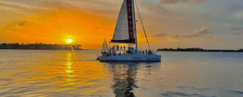 A large catamaran sailing at sunset in Key West with passengers on deck.